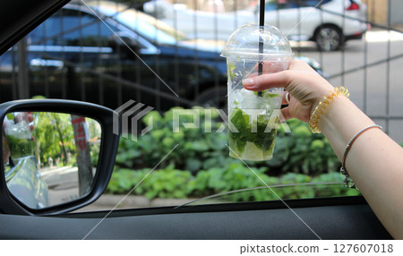 A glass with a cocktail in the hand of a woman leaning out of a car window A glass with a cocktail in the hand of a woman leaning out of a car window 127607018