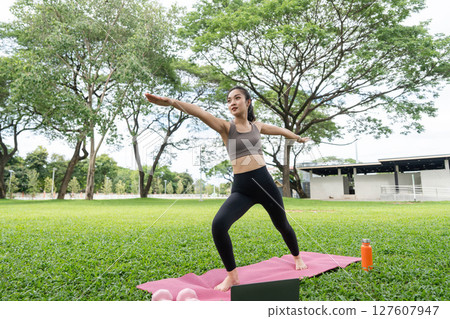 Dynamic yoga practice outdoors. Woman demonstrating strength and flexibility in a park. Dynamic yoga practice outdoors. Woman demonstrating strength and flexibility in a park. 127607947