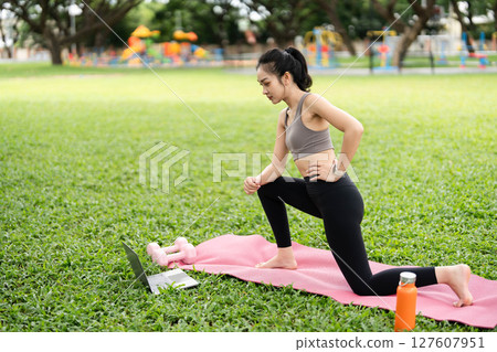 Yoga and Online Fitness. Young woman practicing yoga stretches outdoors using a laptop. 127607951