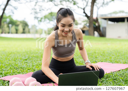 Yoga and technology. A woman engages in yoga practice while using a laptop outdoors. 127607967