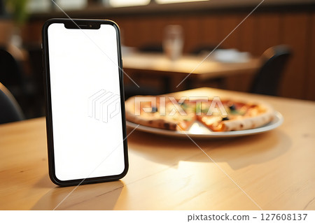 A cell phone is sitting on a table next to a pizza 127608137