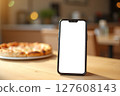 A cell phone is sitting on a table next to a pizza 127608143