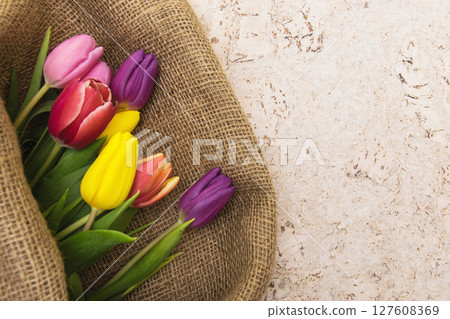 Multicolor tulips bouquet in natural fabric wrapping paper. Spring flowers on the cork background . Top view with place for text. Copy space. Multicolor tulips bouquet in natural fabric wrapping paper. Spring flowers on the cork background . Top view with place for text. Copy space. 127608369