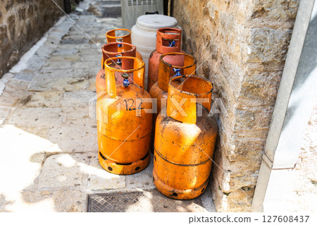 Old gas cylinders stand in a narrow stone alley under the summer sun. Urban infrastructure, fuel storage, and rustic street atmosphere 127608437