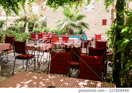 Charming outdoor cafe with red checkered tablecloths in a Mediterranean courtyard. Summer ambiance, hospitality and peaceful dining Charming outdoor cafe with red checkered tablecloths in a Mediterranean courtyard. Summer ambiance, hospitality and peaceful dining 127608440