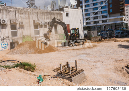 Excavator working at urban construction site. Civil engineering, city development, and modern infrastructure progress. 127608486