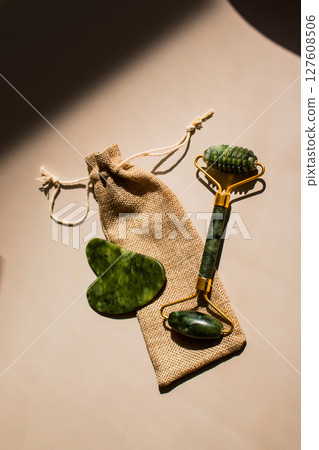 Jade roller and gua sha tools arranged artistically on soft beige background, showcasing natural beauty products for skincare and wellness routines. 127608506