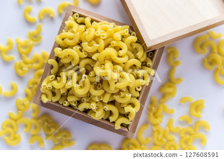 Italian food concept and menu design. Uncooked yellow pasta in wood box on white background. Flat lay. Top view. Italian food concept and menu design. Uncooked yellow pasta in wood box on white background. Flat lay. Top view. 127608591