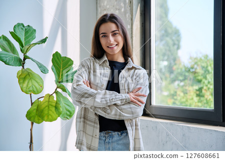 Portrait of confident successful teenage girl posing with crossed arms near window 127608661