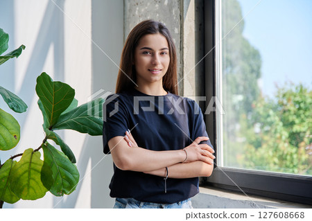Portrait of confident successful teenage girl posing with crossed arms near window 127608668