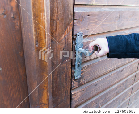 Man holding old metal door handle on the wood door. Vintage iron pen. Man holding old metal door handle on the wood door. Vintage iron pen. 127608693