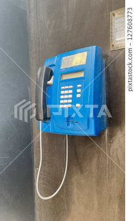 Old blue payphone mounted on a weathered wall, serving as a relic of past communication in a secluded urban area 127608773