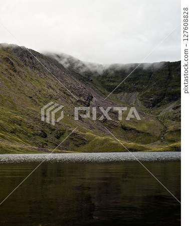 Serene mountain lake framed by imposing cliffs and misty peaks, a breathtaking landscape of contrasts. Serene mountain lake framed by imposing cliffs and misty peaks, a breathtaking landscape of contrasts. 127608828