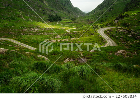 A winding road meanders through rolling hills and towering mountains; a journey awaits. 127608834