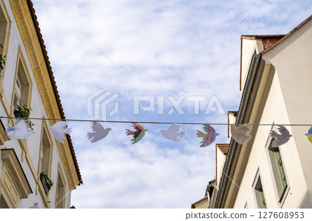 Colorful Paper Birds Gracefully Hanging Between Buildings Beneath a Bright Blue Sky Space Colorful Paper Birds Gracefully Hanging Between Buildings Beneath a Bright Blue Sky Space 127608953
