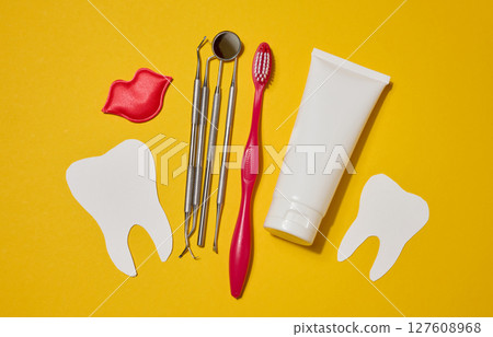 Red toothbrush, white tube of toothpaste, red decorative lips, dental instruments, dental floss in a case and white paper teeth cut out on a yellow background. Red toothbrush, white tube of toothpaste, red decorative lips, dental instruments, dental floss in a case and white paper teeth cut out on a yellow background. 127608968