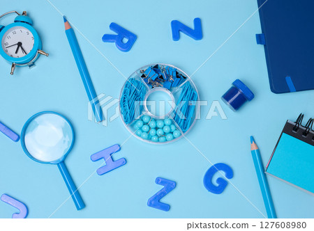Flat lay of blue stationery, learning items letters, magnifying glass, supplies, and an alarm clock on a blue background. 127608980