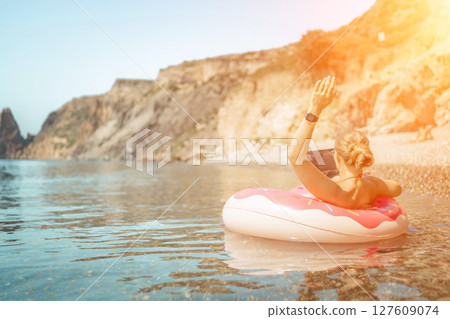 Woman laptop sea. Freelancer woman in sunglases floating on an inflatable big pink donut with a laptop in the sea. People summer vacation rest lifestyle concept 127609074