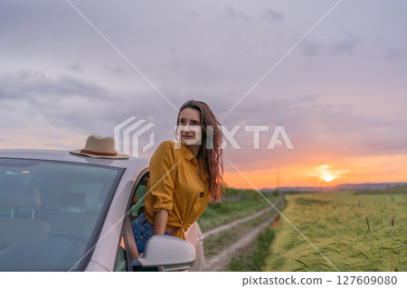 A woman in a yellow shirt is sitting in a car with a straw hat on 127609080