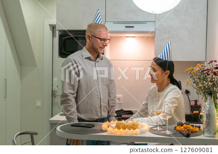 Couple Birthday Celebration Kitchen: Man Woman enjoying birthday cake, candles, party hats in modern apartment kitchen at night. Couple Birthday Celebration Kitchen: Man Woman enjoying birthday cake, candles, party hats in modern apartment kitchen at night. 127609081