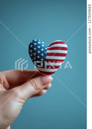 Hand Holding Heart-Shaped Stars and Stripes Object on Blue Background 127609668