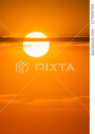 Sun glowing through thin clouds in vibrant orange sky at sunrise or sunset, creating a warm, dreamy atmosphere 127609709
