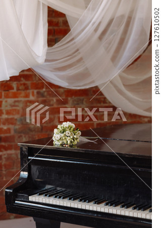 Wedding rings and white rose bouquet on black piano in rustic room with brick wall 127610502