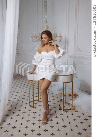 Young woman in white dress posing near table in classic white room with tiled floor and lemons 127610503