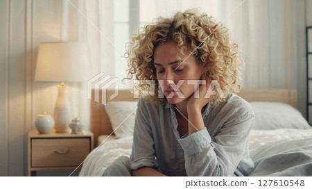 a sad woman sitting on her bed 127610548