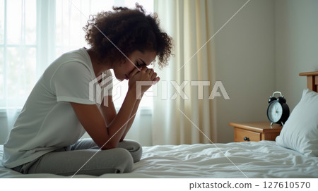 a sad woman sitting on her bed 127610570