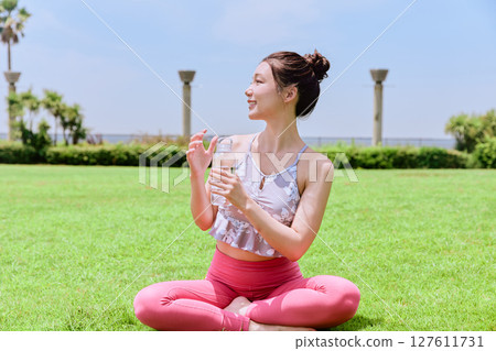 A healthy woman hydrating after yoga on natural grass under the blue sky A healthy woman hydrating after yoga on natural grass under the blue sky 127611731