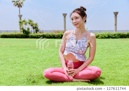 A healthy woman hydrating after yoga on natural grass under the blue sky 127611744