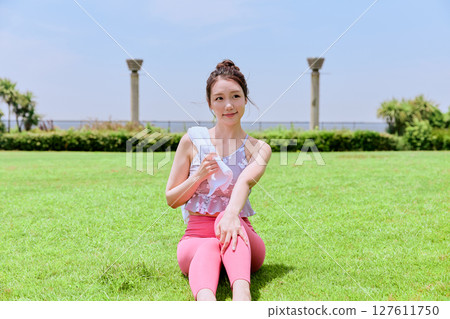 一位身穿瑜珈服的女子在藍天下的天然草地上擦汗 127611750