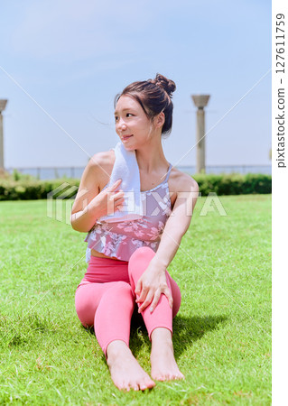 A woman in yoga wear wipes sweat on natural grass under a blue sky A woman in yoga wear wipes sweat on natural grass under a blue sky 127611759