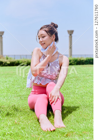 A woman in yoga wear wipes sweat on natural grass under a blue sky 127611760