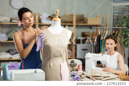 Woman tailor connects parts of dress on mannequin, female craftsman tailor work and sewing 127612033