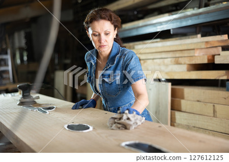 During manufacturing, woman employee grinds surface of wooden board, gives smoothness to surface 127612125