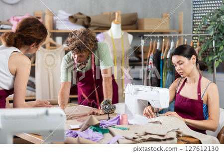 Female and male dressmakers drawing with curves and talking while other sewing 127612130
