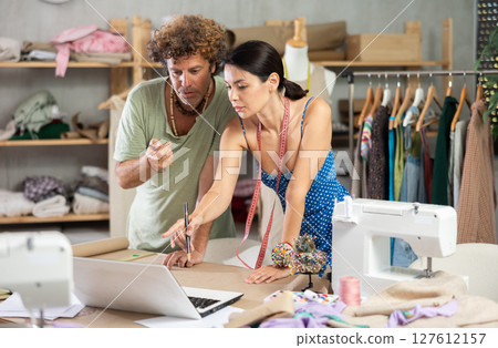 Female and male dressmakers drawing on paper and talking Female and male dressmakers drawing on paper and talking 127612157