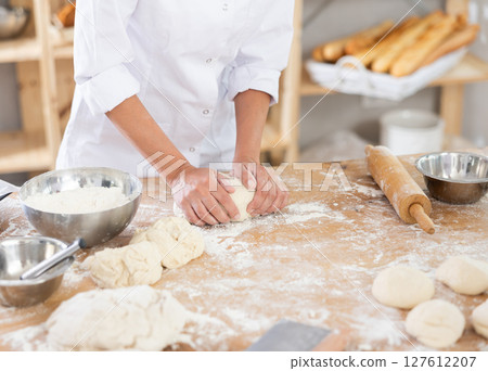 Cute doughs arranged on table in bakery with close-up of woman's hands skillfully kneading dough at food production line 127612207
