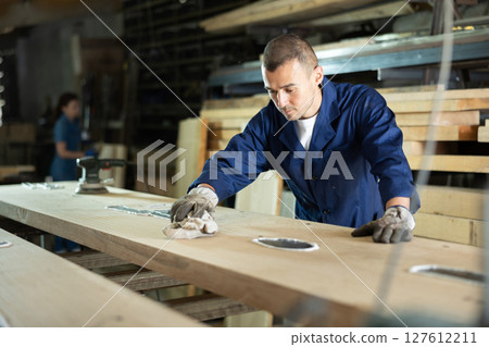 Young man wipes oak plank in workshop Young man wipes oak plank in workshop 127612211