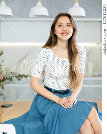 Portrait of young housewife in blouse and denim skirt posing in kitchen 127612226