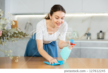 Positive middle-aged woman cleaning the surface of kitchen table Positive middle-aged woman cleaning the surface of kitchen table 127612245