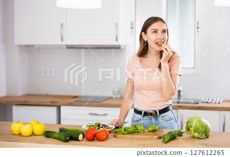 Woman tasting vegetable while cooking salad at home Woman tasting vegetable while cooking salad at home 127612265