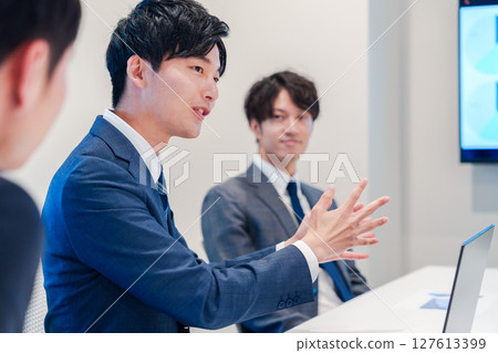 A young male businessman speaking at a meeting A young male businessman speaking at a meeting 127613399