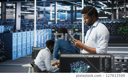 Data center engineer using tablet to interpret AI generated data analytics graphs. Server room worker using artificial intelligence displaying system performance predictive metrics, camera A 127613500