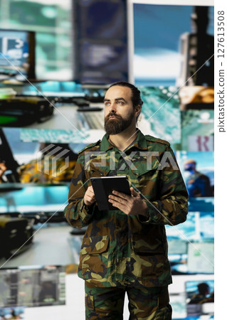 Young soldier working in command center with satellite surveillance integrating data, intelligence and AI warfare tactics for war planning in a national defense mission. Armed forces. 127613508