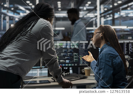 Data center software developers using PC to visualize artificial intelligence neural networks. Server room team leader and worker looking at computer monitor, working together to oversee AI systems Data center software developers using PC to visualize artificial intelligence neural networks. Server room team leader and worker looking at computer monitor, working together to oversee AI systems 127613558
