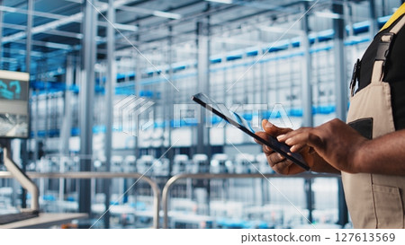 Smart factory expert using digital device app to test automated systems and ensure reliability. Worker uses tablet to identify bottlenecks and optimize gear based on sensors data, camera A close up Smart factory expert using digital device app to test automated systems and ensure reliability. Worker uses tablet to identify bottlenecks and optimize gear based on sensors data, camera A close up 127613569