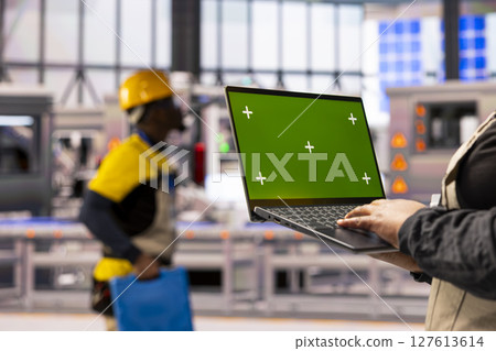 Industry 4.0 expert holding laptop with isolated chromakey template in smart manufacturing plant. The automated factory uses digital interfaces, robotic arms and advanced assembly line. 127613614